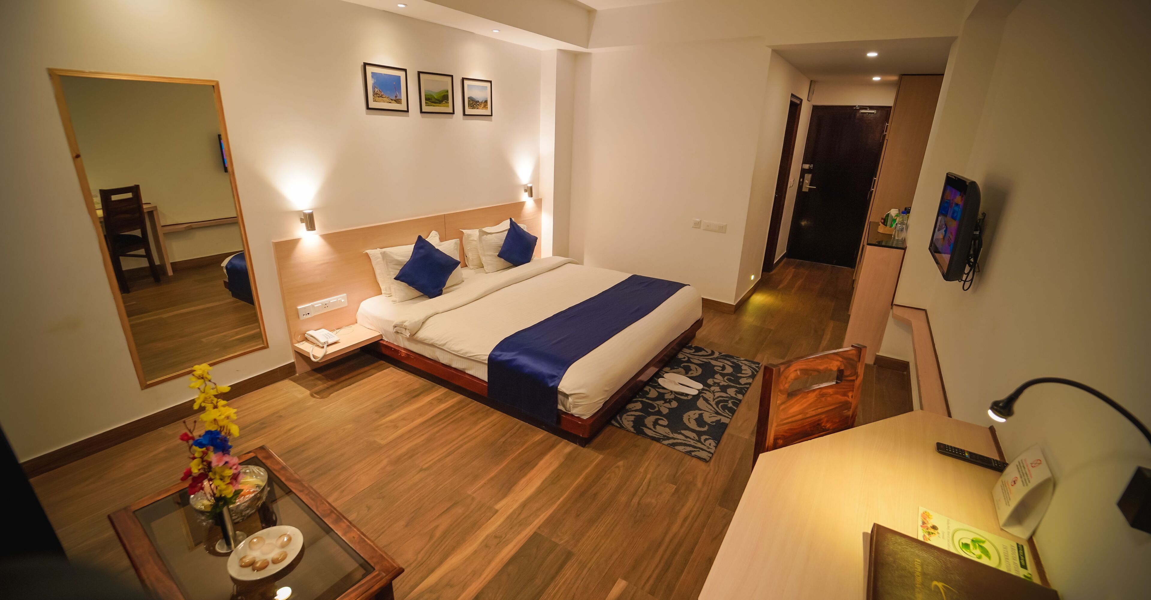 A hotel room with a large bed, bedside tables, a desk, a chair, a mirror, and a door leading to a hallway.