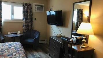 Habitación de hotel con cama, escritorio, silla, televisión, lámpara y ventana con cortinas.