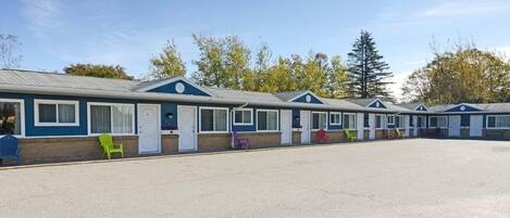 A row of mobile homes with a gravel parking area and a clear sky.