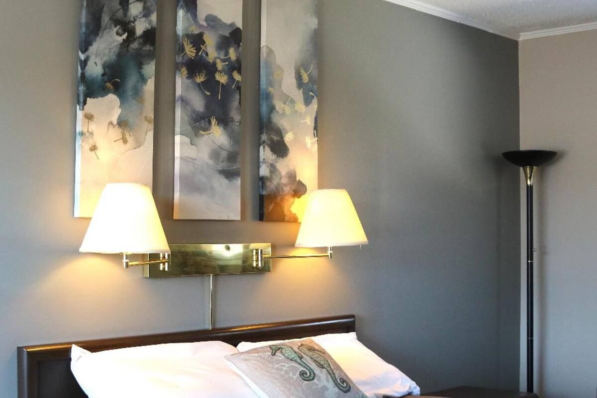 Ein Hotelzimmer mit einem Bett, zwei Wandleuchten und drei abstrakten Bildern an der Wand.