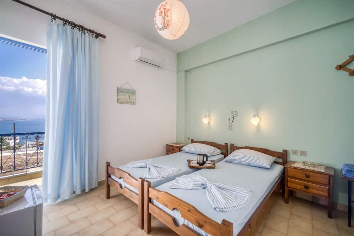 A double bed with striped towels, a bedside table, a nightstand, a wall-mounted light, and a view of the sea.