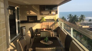 A balcony with a dining table and chairs, a small kitchen area, and a view of the beach and ocean.