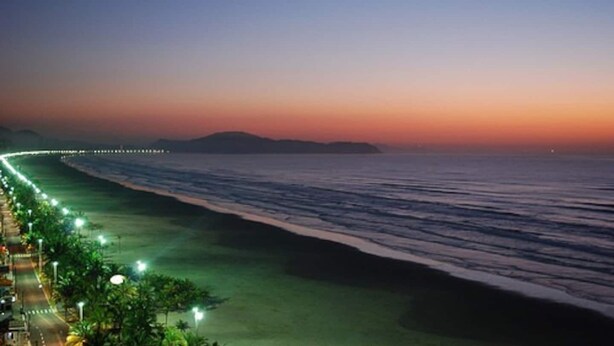 A coastal road with street lighting and a view of the ocean at sunset.