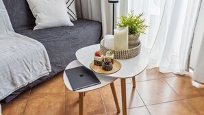 A modern living room with a grey sofa, a small round table with a laptop, a candle, and a plant. - GGK Apartments -O- (Heraklion)