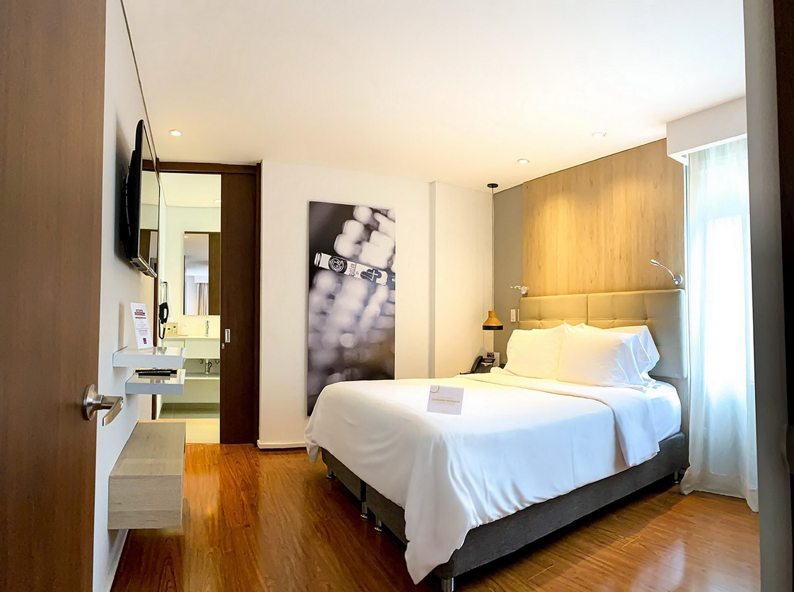 Une chambre d’hôtel équipée d’un lit, d’une table de chevet, d’une lampe et d’un téléviseur fixé au mur.