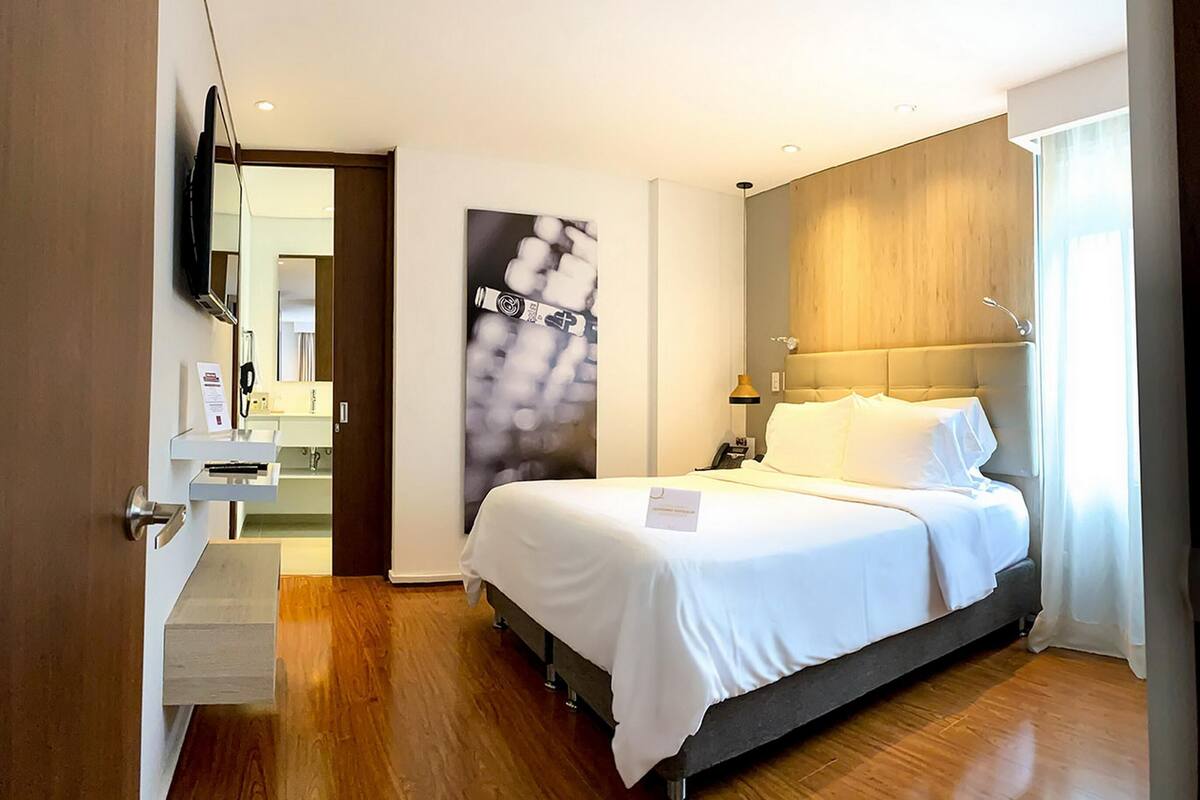 Une chambre d’hôtel équipée d’un lit, d’une table de chevet, d’une lampe et d’un téléviseur fixé au mur.