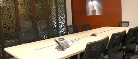 Una sala de conferencias con una larga mesa, varias sillas, un teléfono y un panel decorativo con una lámpara.