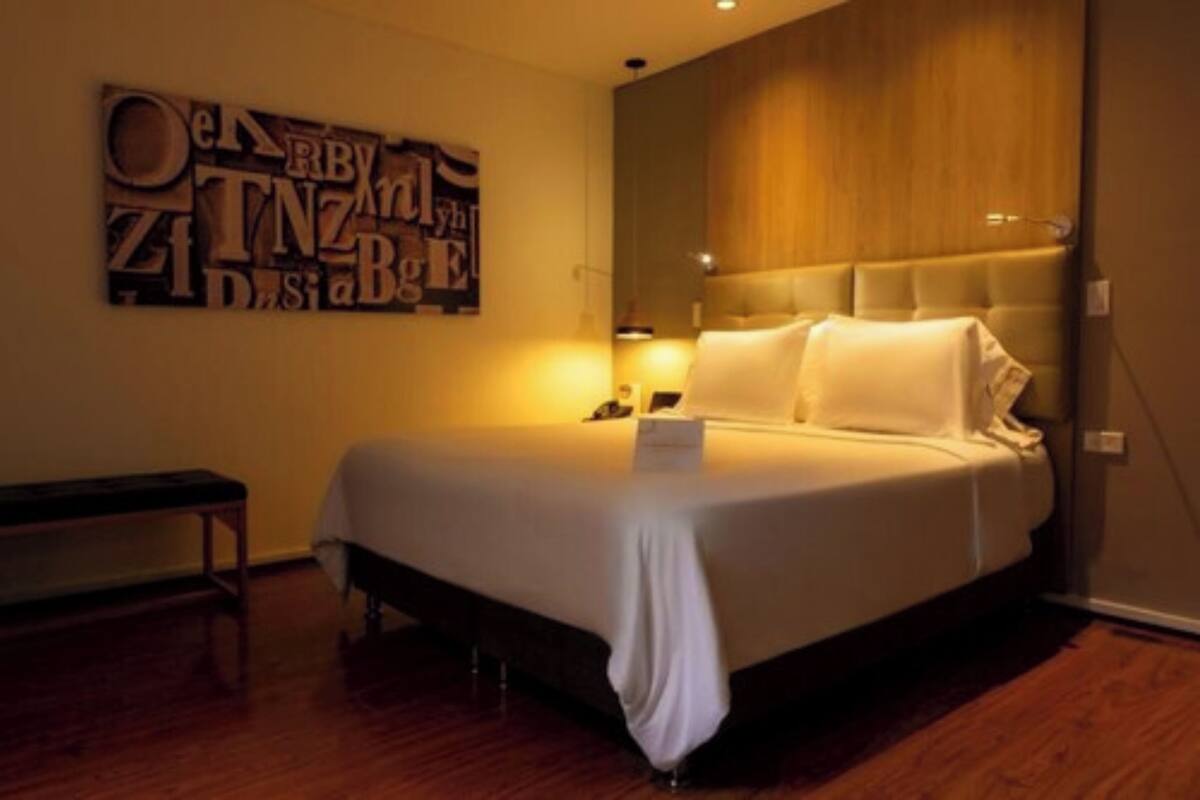 Un lit bien fait dans une chambre d’hôtel, avec une tête de lit en bois, une table de chevet et une œuvre d’art accrochée au mur au-dessus du lit.