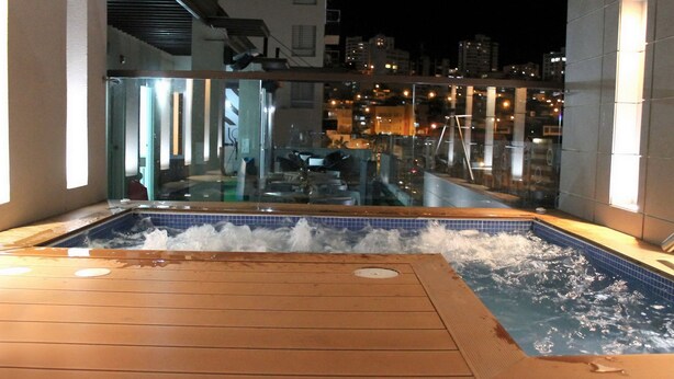 A hot tub area with a wooden deck, glass walls, and a city view at night. - Hotel Quo Quality Manizales (Manizales)