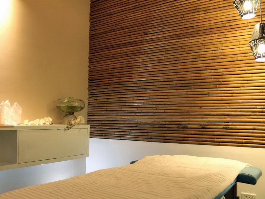 Una habitación con cama, una mesita de noche con un florero y una pared con listones de madera horizontales.
