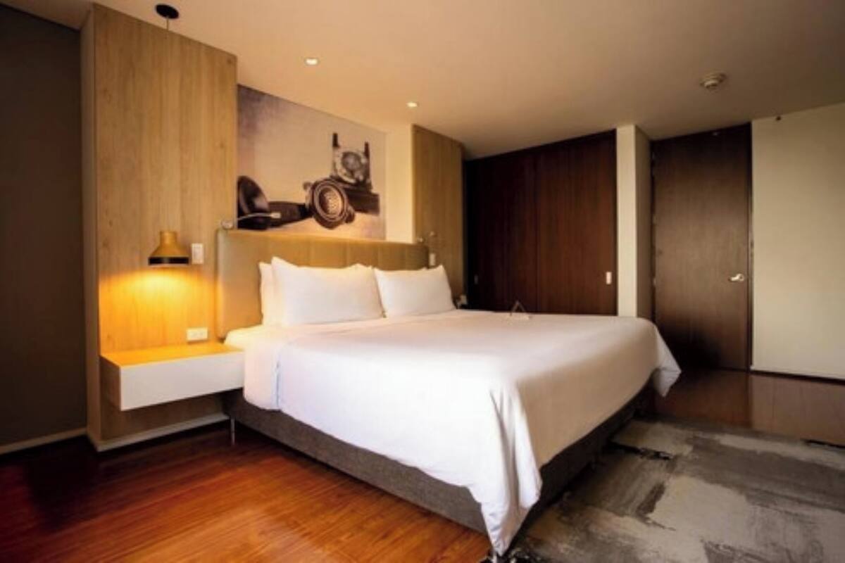 Une chambre moderne avec un grand lit, une table de chevet, une horloge murale et un panneau en bois sur le mur de gauche.