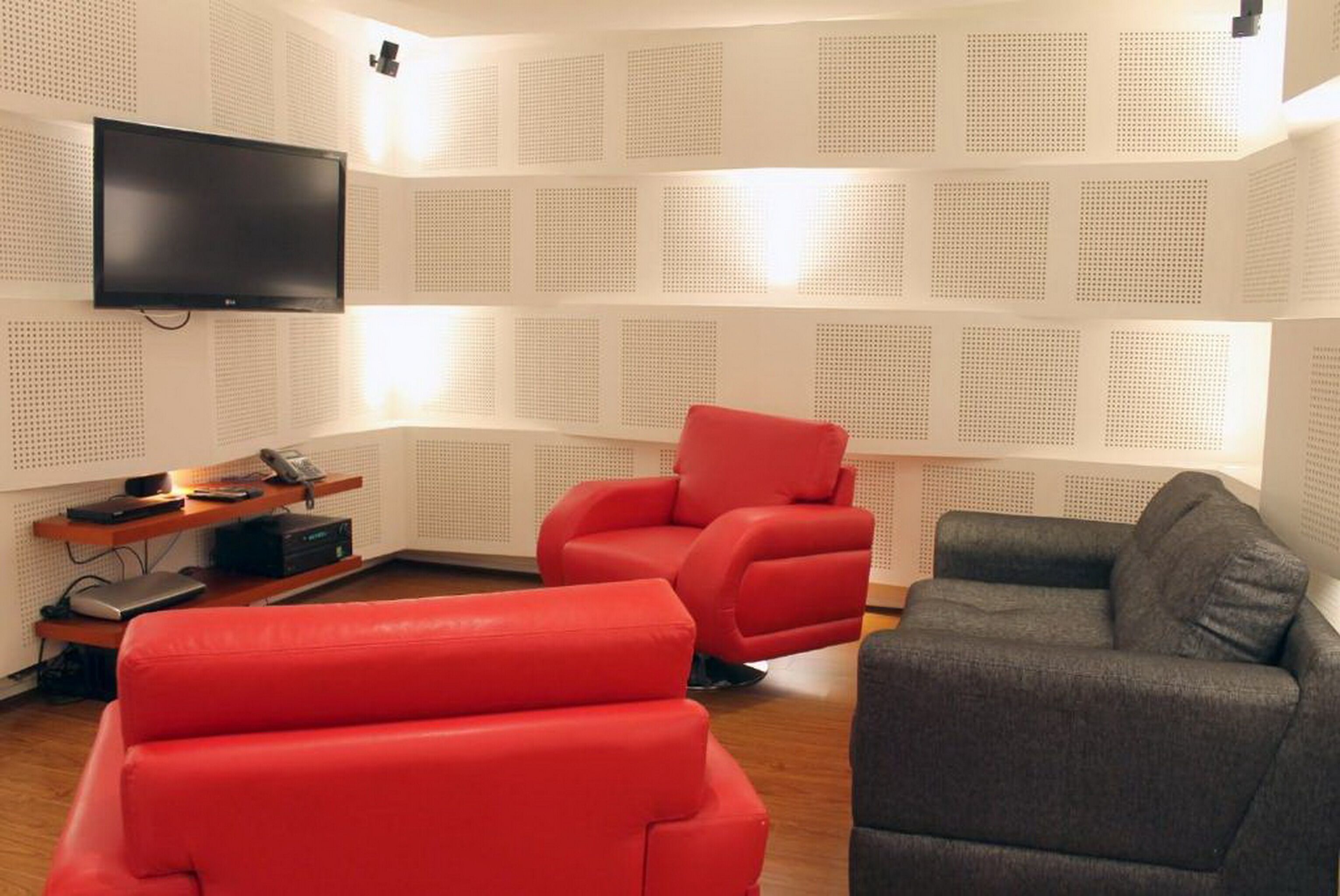Un soggiorno moderno con una televisione a schermo piatto montata al muro, una poltrona rossa, un divano grigio e un tavolino da caffè in legno.