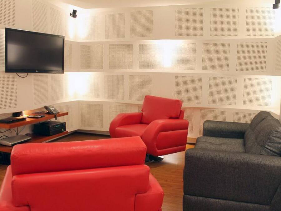 Una sala moderna con un televisor de pantalla plana montado en la pared, un sillón rojo, un sofá gris y una mesa de centro de madera.