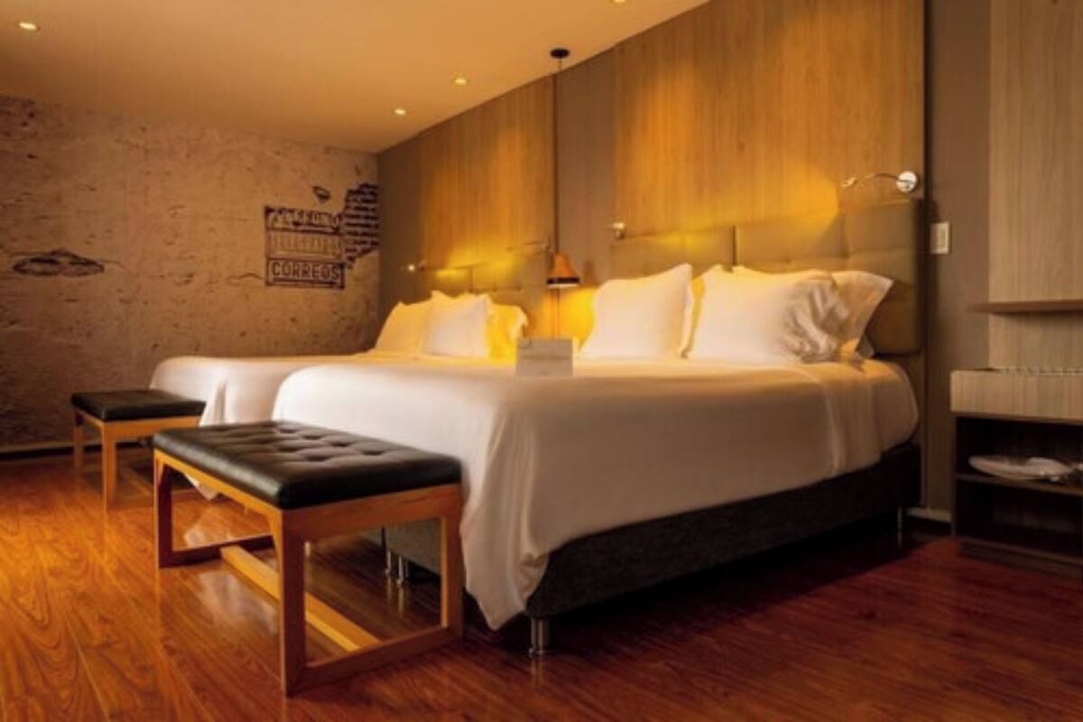Une chambre d’hôtel moderne avec un grand lit, deux tables de chevet et un banc.