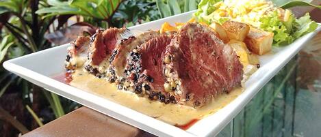 A plate of sliced meat with a creamy sauce, accompanied by roasted potatoes and a side salad.