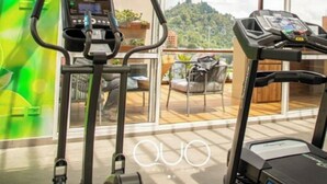 A gym with two treadmills and a stationary bike, large windows, and a view of a mountain. - Hotel Quo Quality Manizales (Manizales)