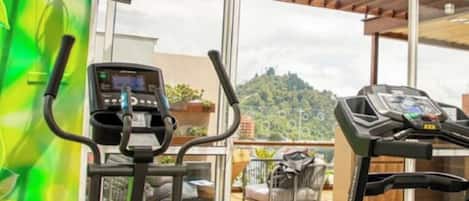 A gym with two treadmills and a stationary bike, large windows, and a view of a mountain.