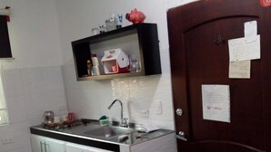 A compact kitchen with white cabinets, a stainless steel sink, and a small countertop. There is a wooden door with a paper note attached. - moskafamily (Cartagena)