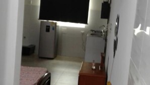 A compact room with a bed, a small desk, a refrigerator, and a window with blinds. - moskafamily (Cartagena)
