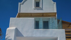 Un edificio blanco con una ventana pequeña y una puerta, con una escalera que conduce a la entrada y una maceta grande en el suelo.