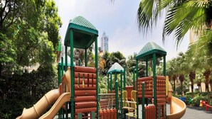 Ein Spielplatz mit Rutschen und Klettergerüsten, umgeben von Bäumen und einem Gebäude im Hintergrund.