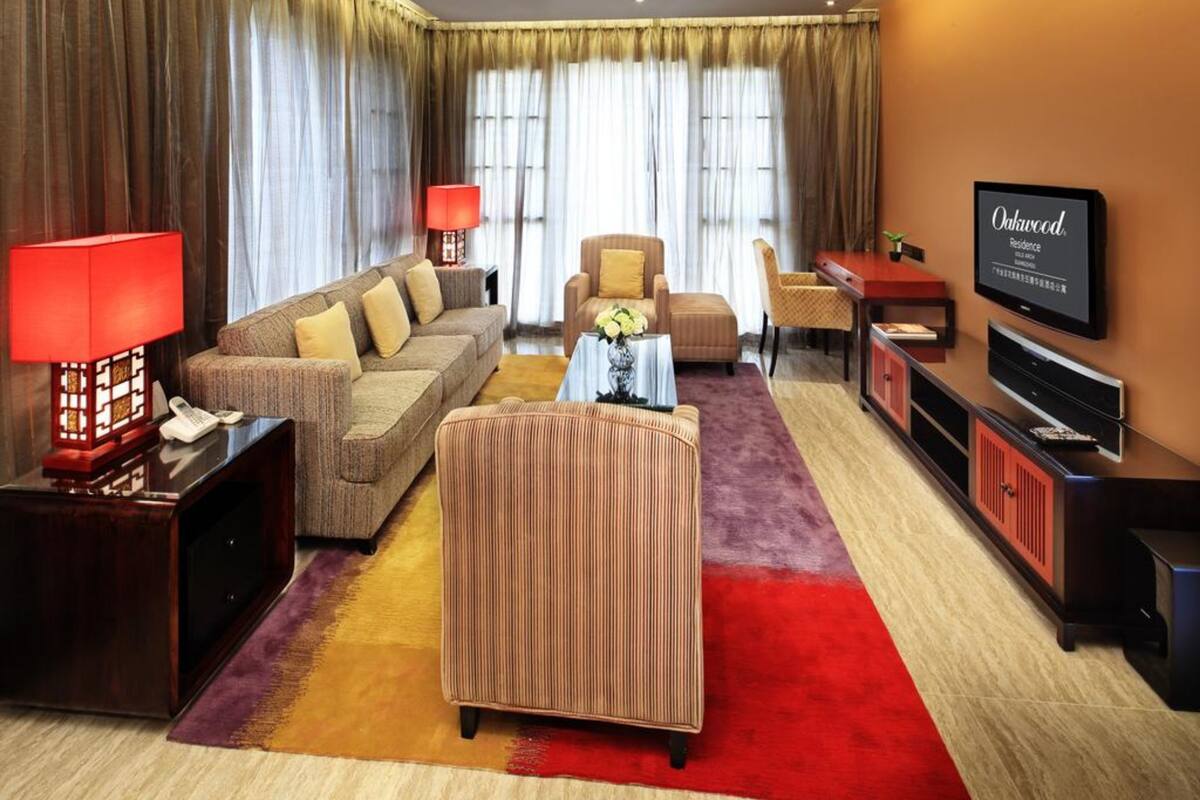 Una sala de estar moderna con un sofá, sillones, una mesa de centro, un televisor y una lámpara roja.