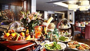 Ein reichhaltiges Buffet mit verschiedenen Speisen, darunter Obst, Salate und Desserts, in einem modernen Essbereich mit Holzboden und zeitgemäßer Einrichtung.