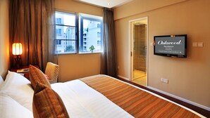 Ein Hotelzimmer mit einem großen Bett, einem an der Wand montierten Fernseher und Blick auf die Stadt durch das Fenster.