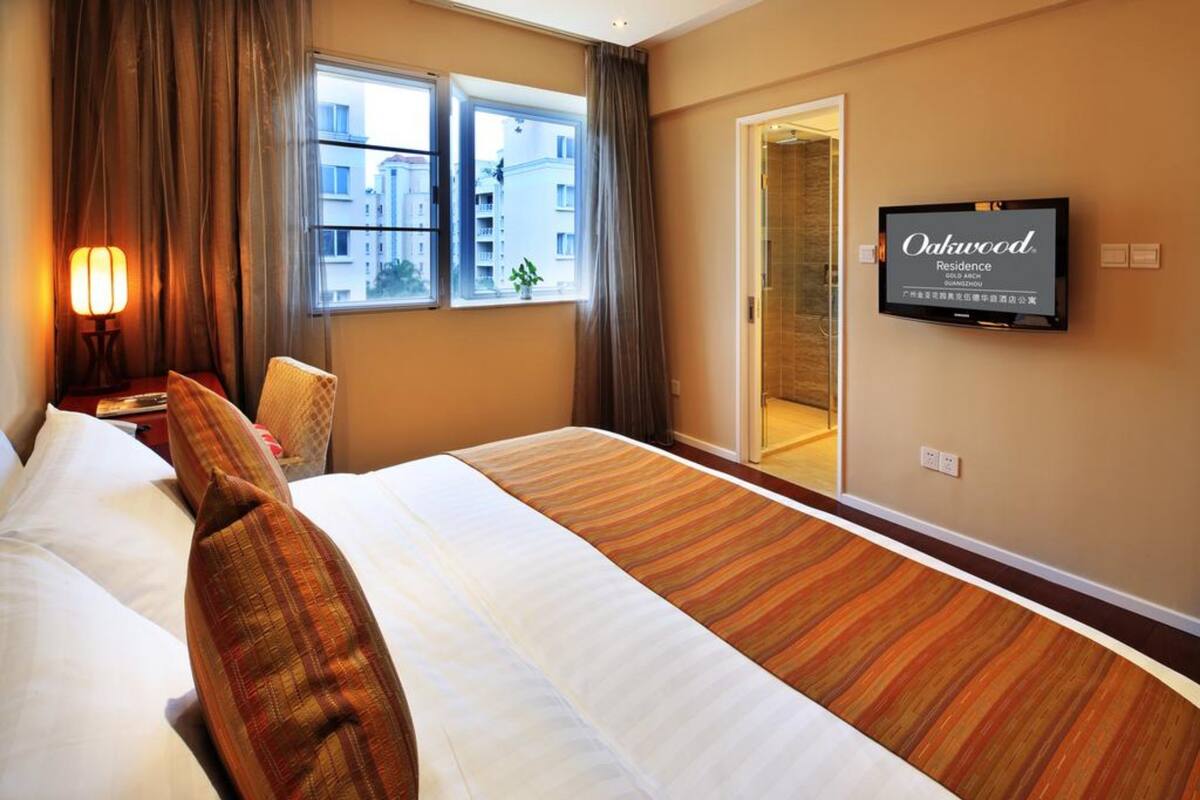 Habitación de hotel con una cama grande, un televisor en la pared y vistas a la ciudad a través de la ventana.