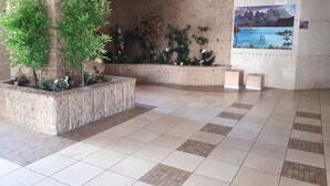 Un'ampia hall con pavimento piastrellato, un'imponente colonna e diverse piante in vaso.