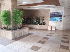 Un hall d’entrée spacieux, doté d’un sol carrelé, d’une grande colonne et de diverses plantes en pot.