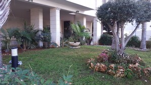 Un edificio con un portico, colonne e un giardino con diverse piante e un albero.