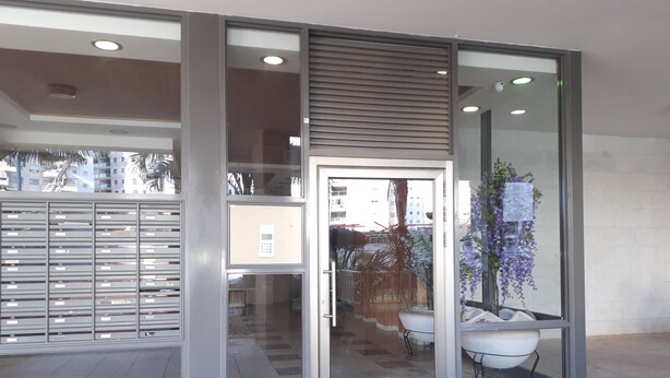 L'ingresso di un edificio moderno con una porta in vetro, armadietti metallici e una pianta in vaso.