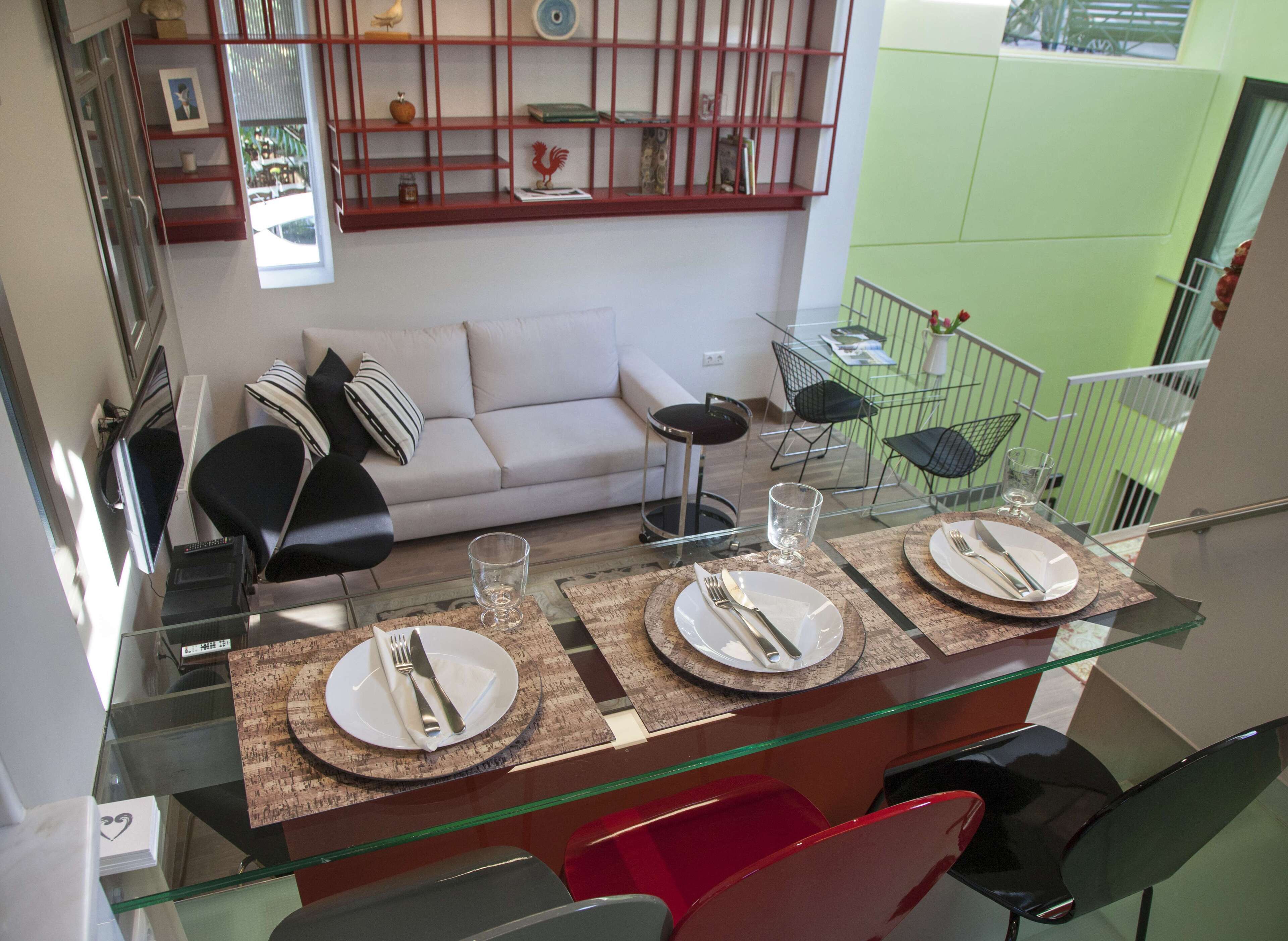 Un coin repas avec une table en verre dressée pour quatre personnes, un canapé et un fauteuil rouge.