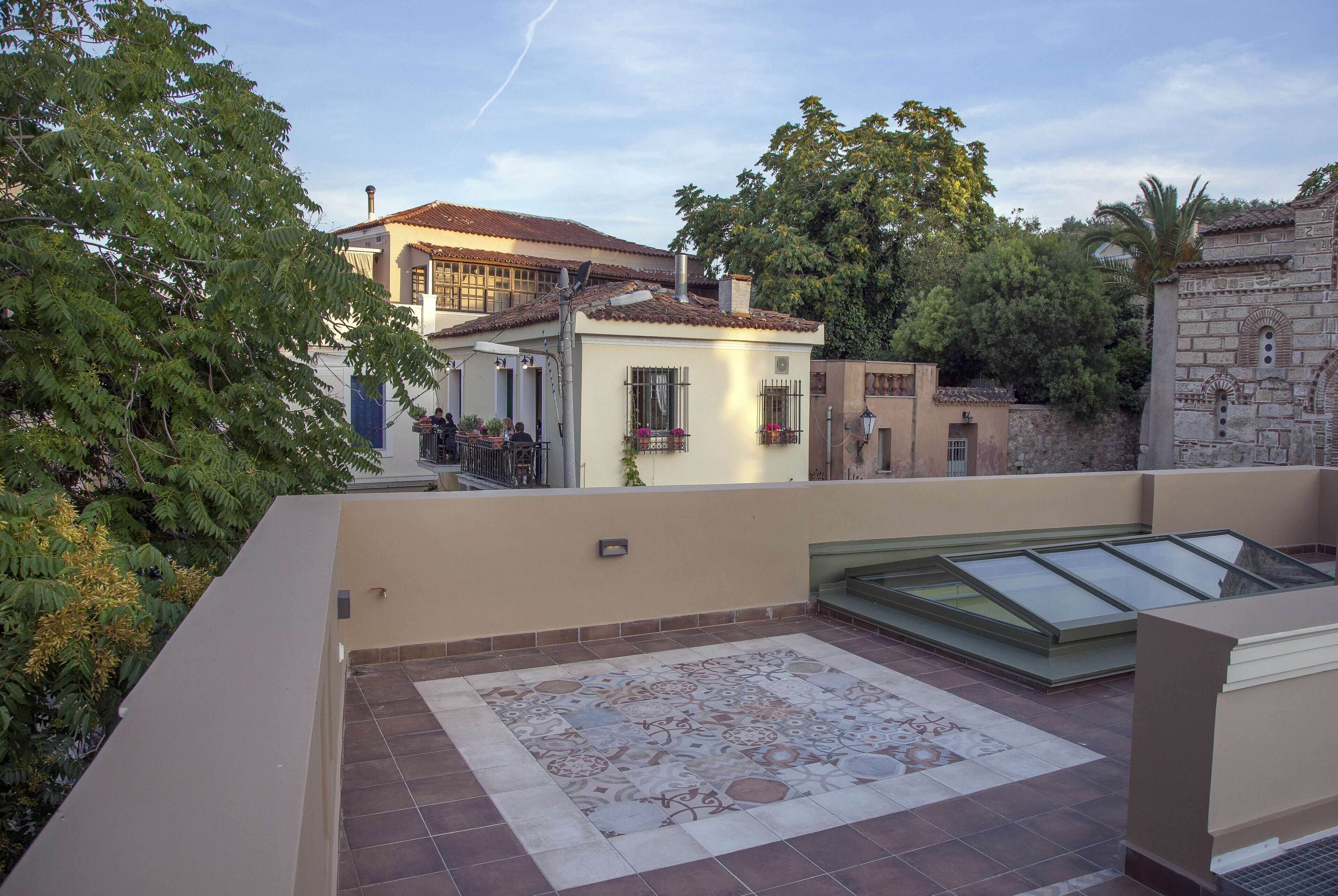 A rooftop terrace with a patterned floor, a glass enclosure, and a view of surrounding buildings.
