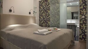 A hotel room with a large bed, a bedside table, a mirror, and a bathroom visible through a glass door. - Tripodon Plaka in the shade of Acropolis by GHH (Athens)