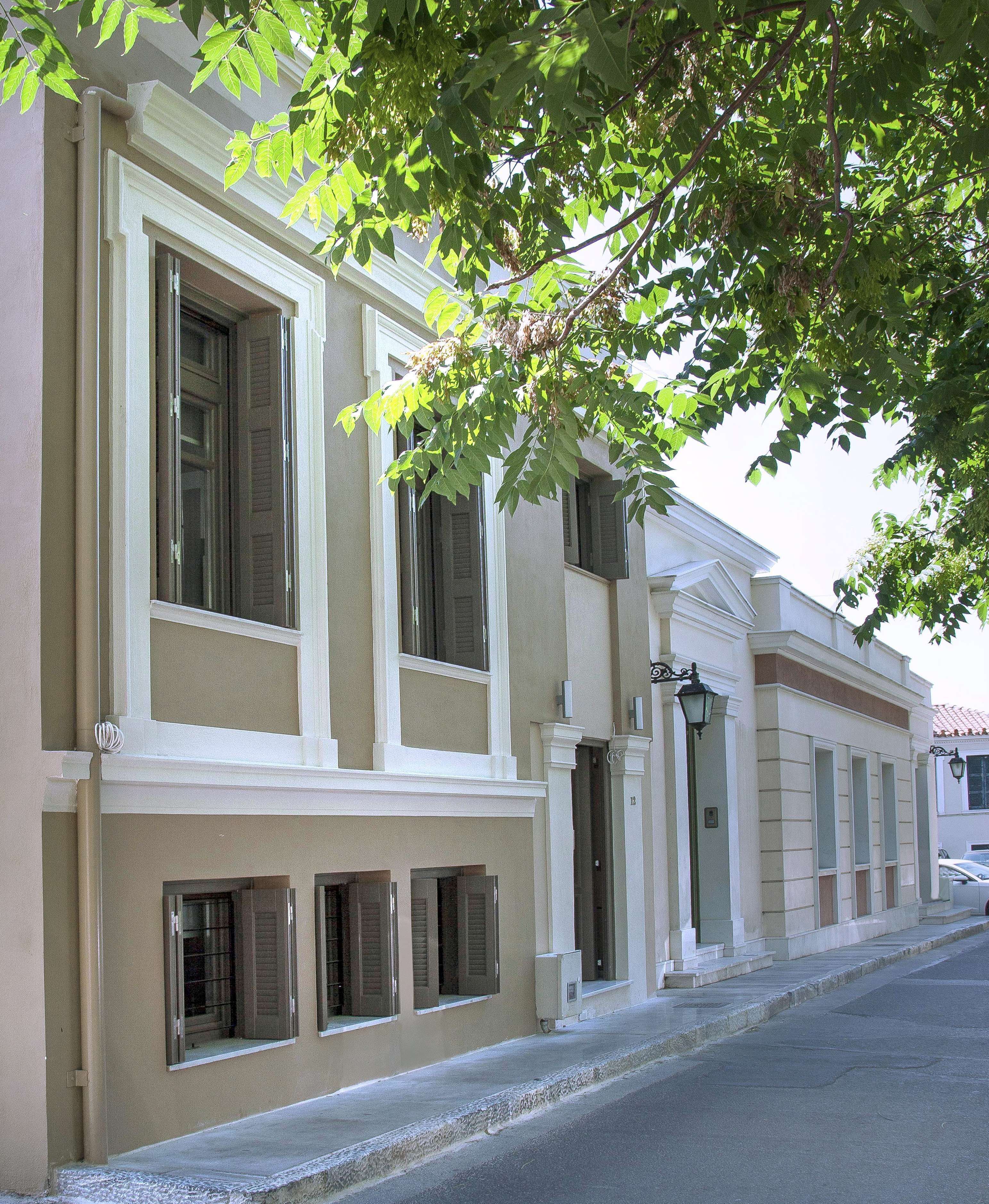 A row of beige buildings with large windows and shutters, a sidewalk, and a street.