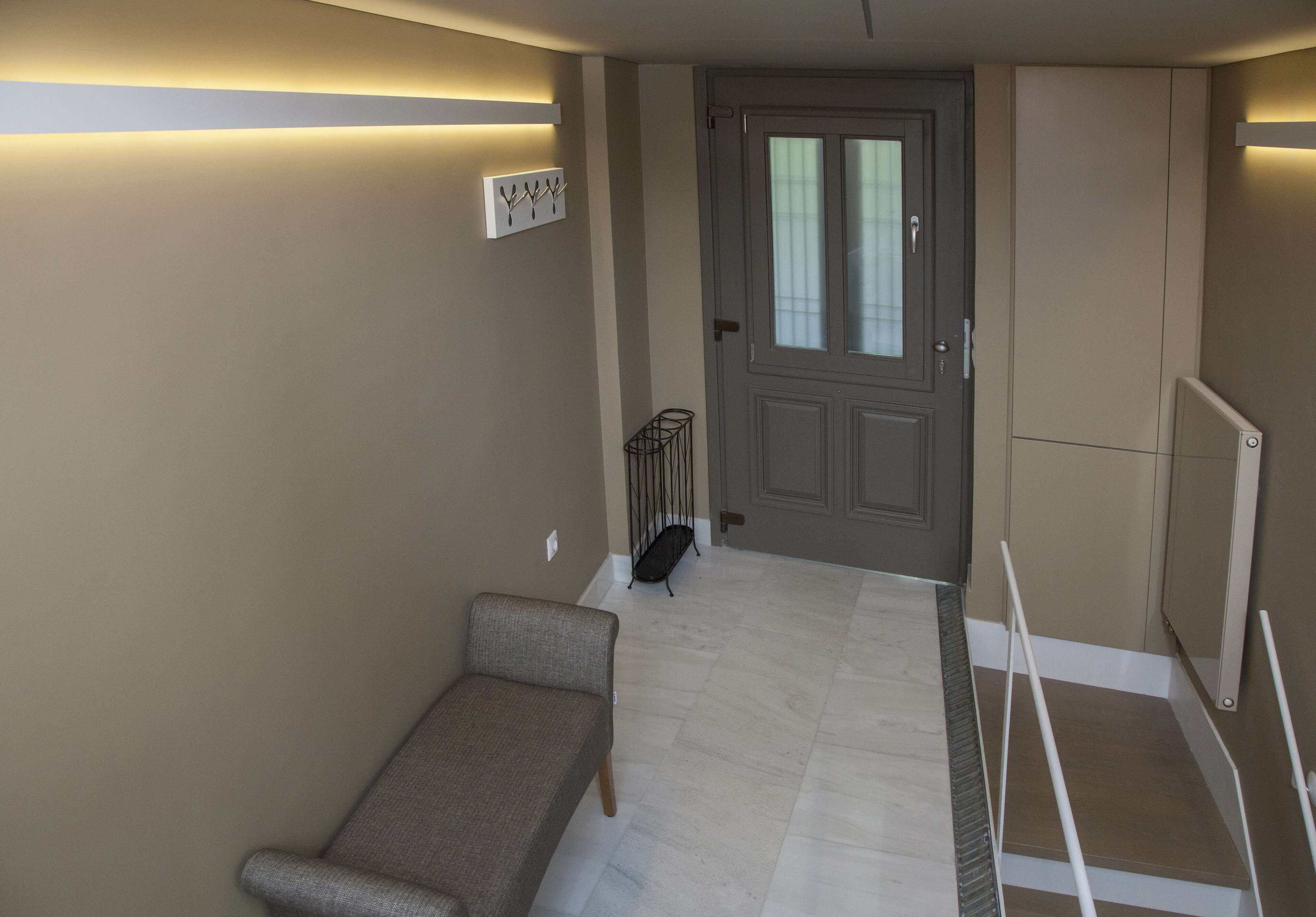 Quarto com um banco, porta com painéis de vidro jateado, cabideiro e radiador.