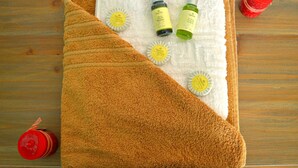 A wooden table with a brown towel, two bottles of lotion, and a red candle. - Sea Horizon Apartments (Ρέθυμνο)