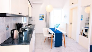 A modern kitchen with a dining area, featuring a kitchen island, white cabinets, and a blue tablecloth-covered table. - Sea Horizon Apartments (Ρέθυμνο)