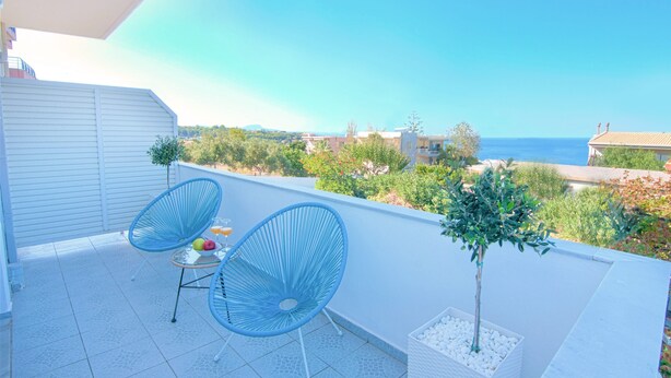 A balcony with two blue chairs, a small table with fruits, and a potted plant. - Sea Horizon Apartments (Ρέθυμνο)