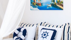 A bed with nautical-themed pillows, a coastal painting, and a white canopy. - Sea Horizon Apartments (Ρέθυμνο)