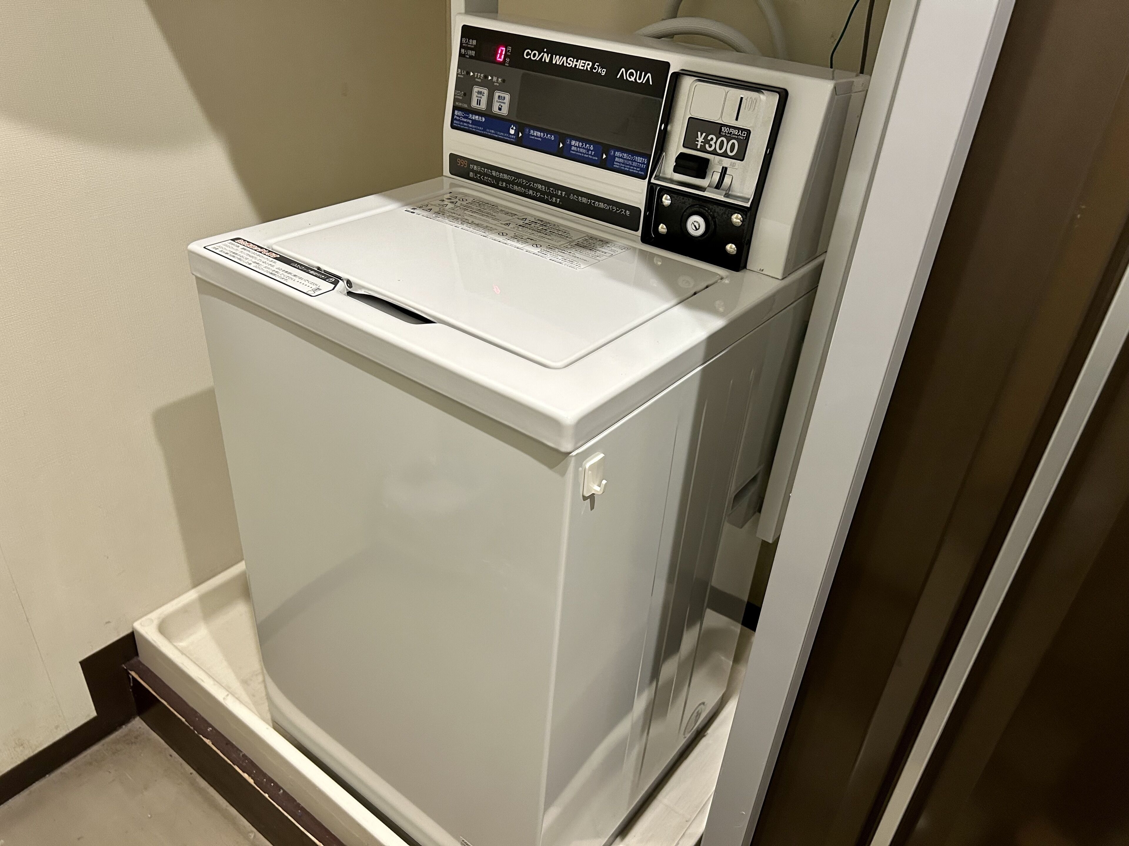 A compact, white coin-operated washer and dryer unit with a digital display and a coin slot.