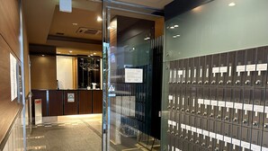 A hotel lobby with a reception desk, a glass door leading to a stairwell, and a wall of numbered lockers. - Cypress Inn Tokyo (Tokyo)