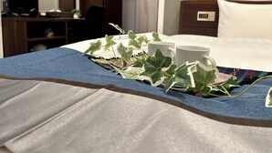 A neatly made bed with a blue blanket, two white mugs, and green leaves on the bedspread. - Cypress Inn Tokyo (Tokyo)