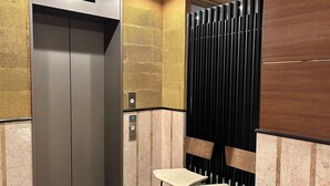 An elevator with a digital display, a textured wall, and two chairs in a modern lobby area. - Cypress Inn Tokyo (Tokyo)