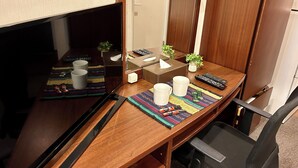 A hotel room with a wooden desk, a television, a mirror, a small plant, a tissue box, and a remote control. - Cypress Inn Tokyo (Tokyo)