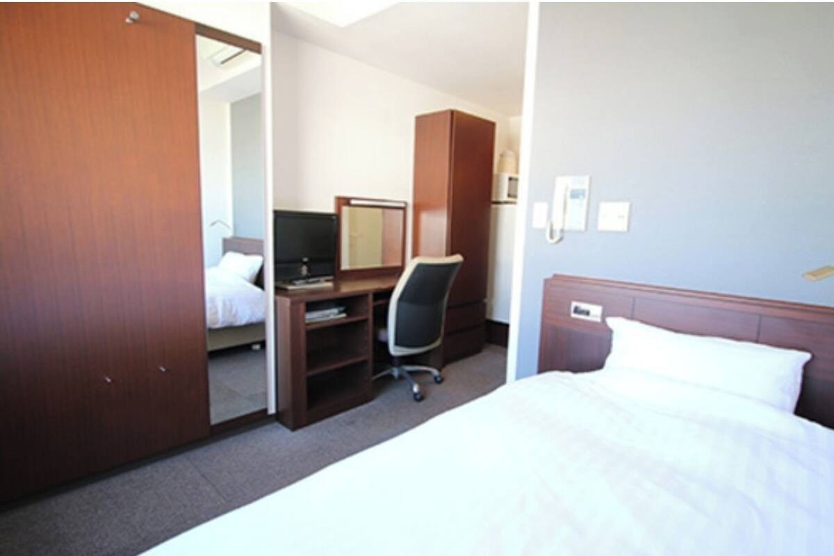 Hotellihuone, jossa on sänky, työpöytä tuolilla, vaatekaappi ja peili.