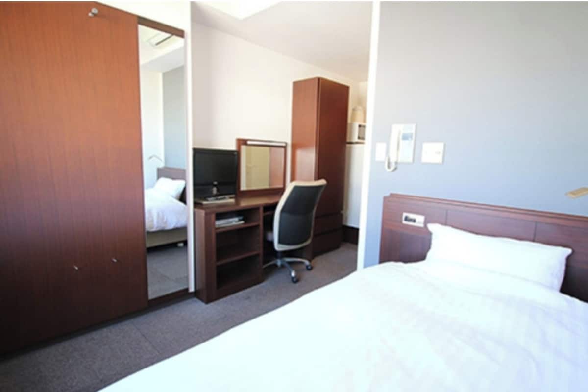 Ein Hotelzimmer mit Bett, Schreibtisch mit Stuhl, Kleiderschrank und Spiegel.