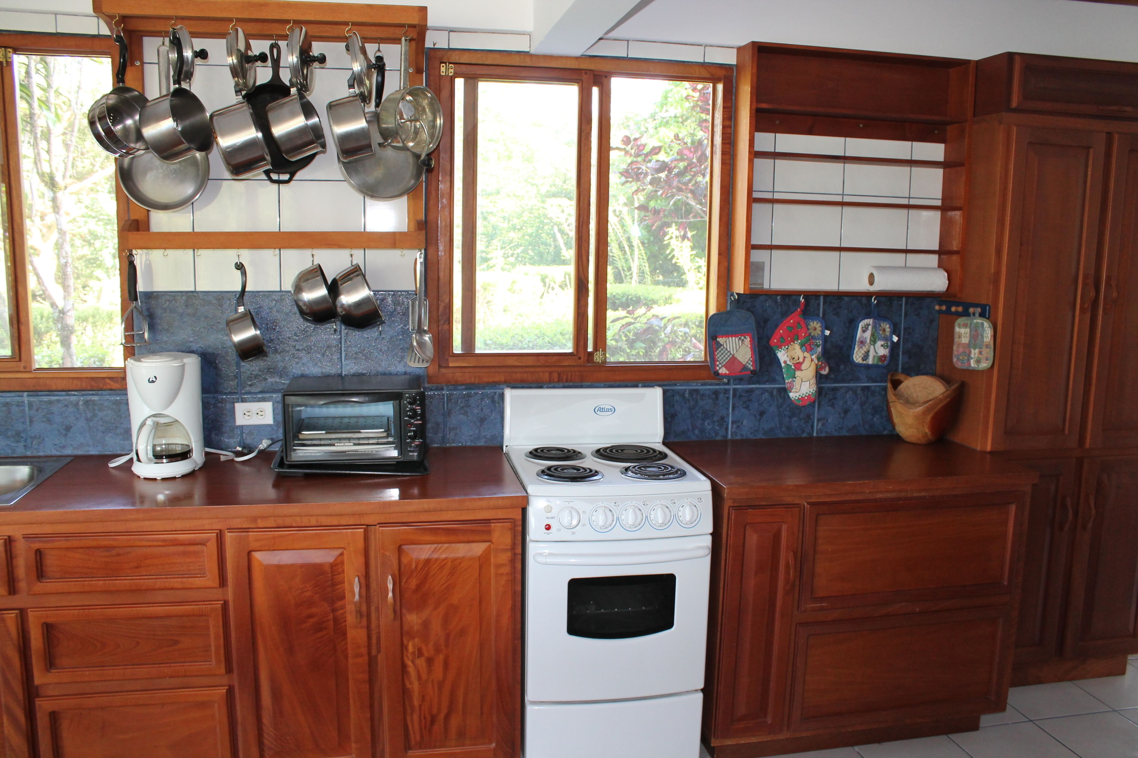 Een keuken met houten kastjes, een fornuis, een koffiezetapparaat en hangende pannen.